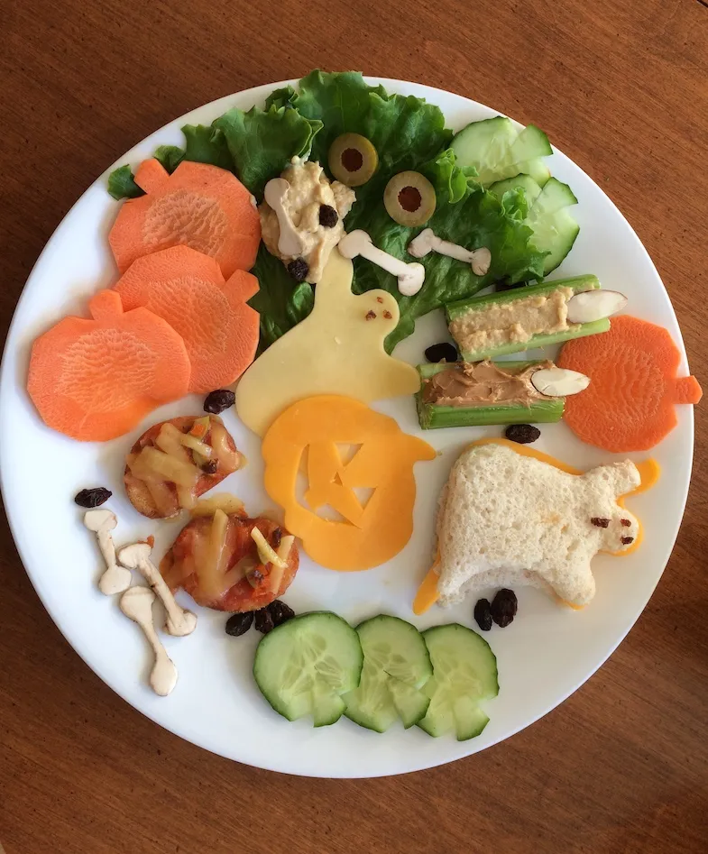 Various gluten-free food in the shapes of halloween shapes, such as, pumpkin carrots, ghost sandwich, witches celery fingers, mushroom bones mummy pizza crackers