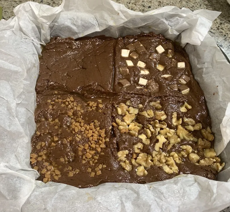 gluten-free milk chocolate fudge in a pan with four different toppings before being put in the fridge