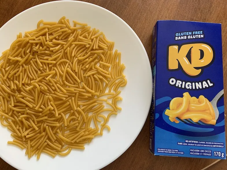 Gluten-free Kraft Dinner with uncooked noodles on a plate beside the package